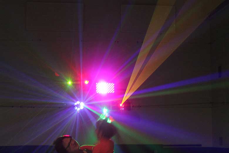 School Light Show, DJ Hamilton, Family Dance Woman holding her child dancing. 2 wide orange beams coming from laser. Several other lights producing a multitude of colors. Taken in Hamilton Ontario.